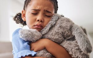 A child worrying and suffering with anxiety clutches her teddy